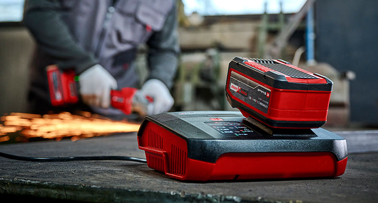 Battery and charger in front of a man working with a cordless angle grinder